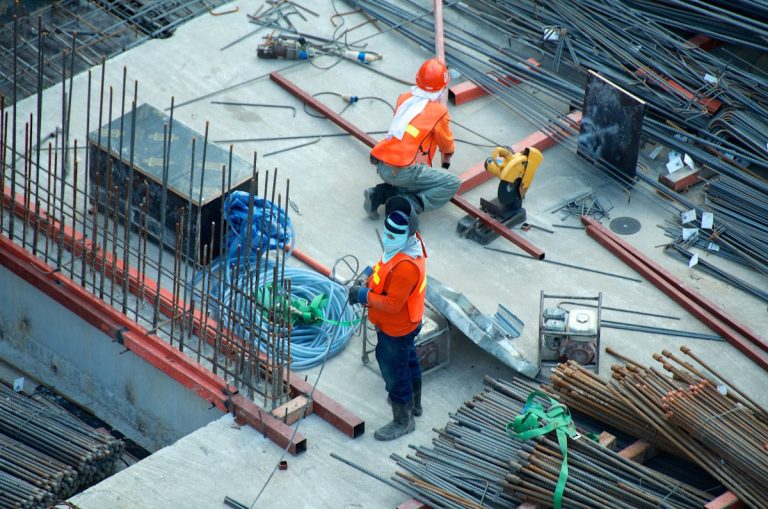 Workers in orange safety gear on a rebar-covered concrete deck, seen from above
